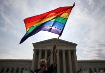 A man holds a six-striped rainbow flag in front of the US Supreme Court.